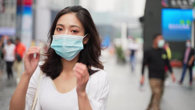Young beautiful Asian girl wearing a mask walking on the street looking back at the camera and smiling slowly taking off the mask. The concept of the end of the epidemic