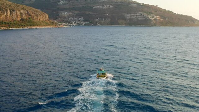 Greece. Mani Laconia, Peloponnese. Fishing boat return to Limeni port aerial tracking shot, bay coast and village. Tourist resort, summer day	