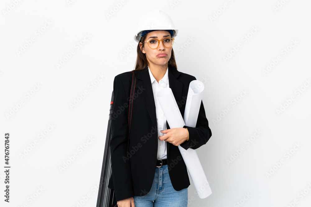 Poster Young architect caucasian woman with helmet and holding blueprints over isolated background sad