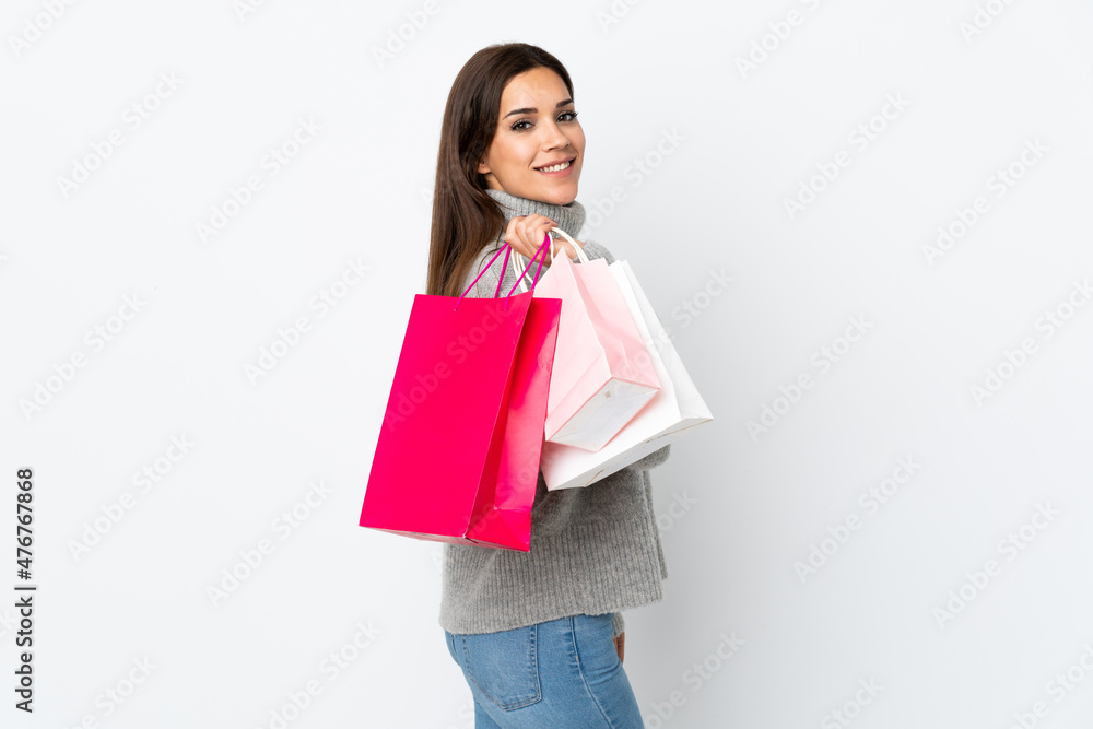 Wall mural Young caucasian woman isolated on white background holding shopping bags and smiling