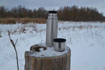 Thermos and a mug on a tree stump in winter.