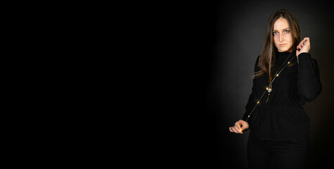 Young girl or woman holding light garlands. She looks at the camera with a focused gaze. Portrait on a black background. Free space for text or signature