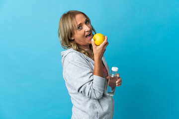 Middle aged blonde woman over isolated background with an apple and with a bottle of water