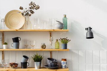 Fototapeta na wymiar Wooden shelves with utensils in modern kitchen with white wall