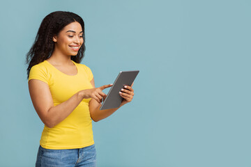 Technologies and entertainment concept. Excited black lady with digital tablet standing on blue background, empty space