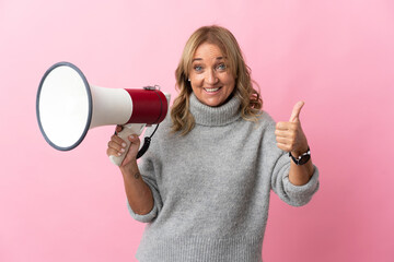 Middle aged blonde woman over isolated pink background holding a megaphone with thumb up