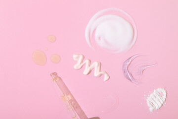 Smears and drops of various cosmetic products and a pipette on pink background. Top view cosmetics