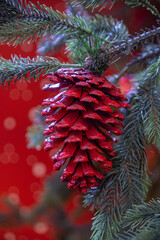 Decorations on a christmas fir-tree: red cone on the blurred red christmas background