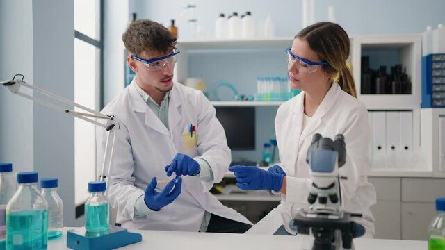 Young couple wearing scientist uniform using microscope working at laboratory