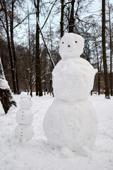 Big and small snowmen in the park in winter - family