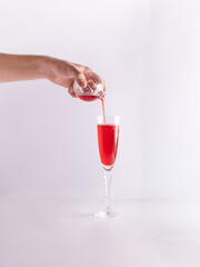Male hand, Christmas decorating bauble, red liquid and Champagne flute glass, creative composition. Happy New Year greeting card. 