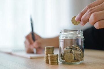 Male hand putting money coin stack and take note of income and expenses for the future growing business, education and retirement. He felt that saving money made his life safe.