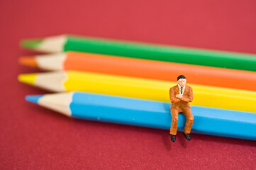 miniature figurine of a man sitting on color pencils - Powered by Adobe