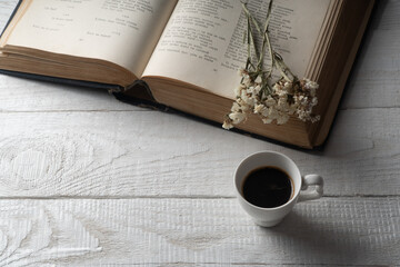 a cup with morning coffee stands near an open book on a white table.