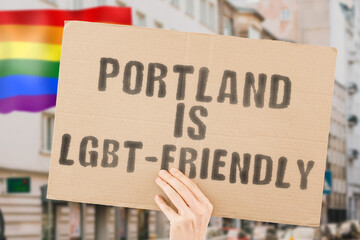 The phrase " Portland is LGBT-Friendly " on a banner in men's hand with blurred LGBT flag on the background. Human relationships. different. Diverse. liberty. Sexuality. Social issues. Society