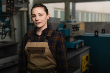 Young welder in uniform looking at camera in blurred factory