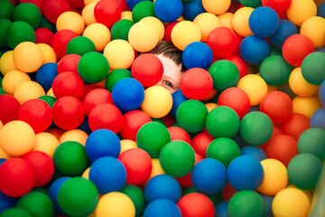 Fototapeta na wymiar A teenage boy, an infante lies buried in balloons in a dry pool, the child is almost invisible among the colorful balloons. A holiday in the entertainment center.