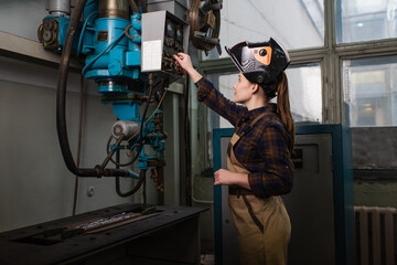 Side view of young welder in mask switching welding machine in factory