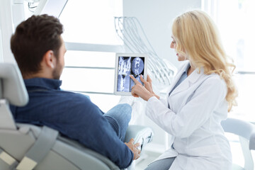 Female dentist showing male patient x-ray on digital tablet
