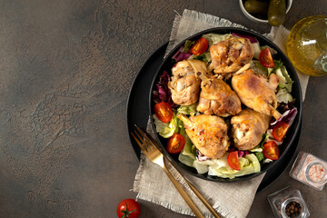 Fried chicken legs with salad in a plate on a dark kitchen table. Cooked poultry meat, pickles, and tomatoes on a culinary background top view	