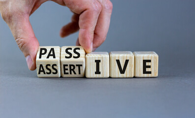 Passive or assertive symbol. Businessman turns wooden cubes and changes the word passive to assertive. Beautiful grey background, copy space. Business, psychological passive assertive concept.