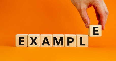 Example symbol. The concept word Example on wooden cubes. Beautiful orange table, orange background, copy space. Businessman hand. Business and example concept.