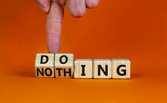 Doing or nothing symbol. Businessman turns wooden cubes and changes the word Nothing to Doing. Beautiful orange background, copy space. Business, doing or nothing concept.