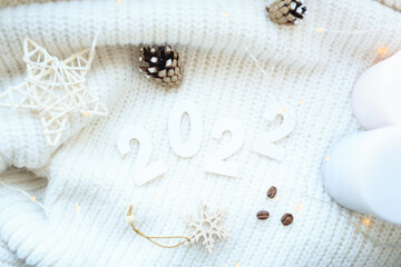 The number 2022 of bokeh in the house on the table with a sweater in the background and decorations. Winter mood, festive decoration, magical Christmas.