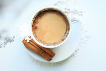 A cup of coffee over Christmas bokeh garlands in the house on the table with a sweater in the background and decorations. Winter mood, festive decoration, magical Christmas.