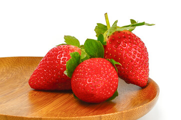 Three fresh strawberries on the wooden plate isolated