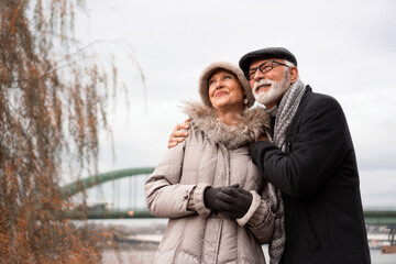 Obraz premium An elderly couple is walking around the waterfront in an urban area. The couple is smiling and looking happy in love.