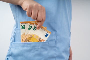 Nurse in blue hospital uniform holds euro banknotes by hand in her pocket
