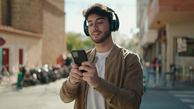 Young hispanic man smiling confident listening to music using smartphone at street