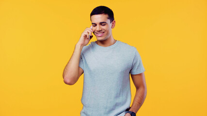 happy young man in t-shirt talking on mobile phone isolated on yellow.