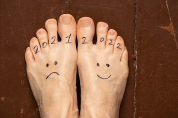 2021 and 2022 sad and joyful smiley painted on the legs of a girl on the wooden floor of the house,...