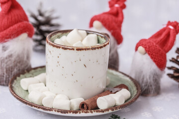 3 Christmas gnomes in red hats  and hot cocoa or coffee with marshmallow in a white ceramic mug close up . The concept of winter drink, cozy holidays and New Year.