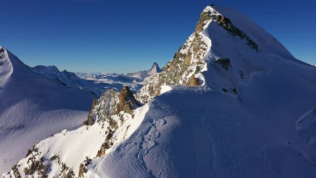 Aerial drone footage of the Allalin peak at 4027m in the Saas-Fee area with the famous Matterhorn in the background in winter in the alps in Canton Valais, Switzerland