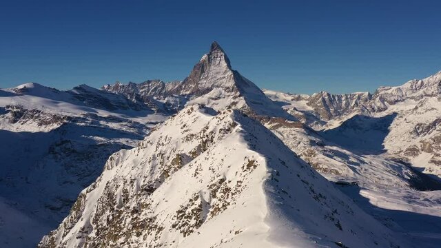 Aerial drone footage of the Matterhorn and the gornergrat ridge with its observatory and hotel above Zermatt in the alps in Switzerland on a sunny winter day. 