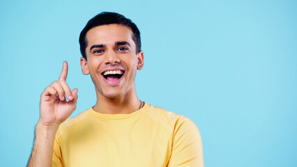 happy young man in yellow t-shirt showing idea sign isolated on blue.