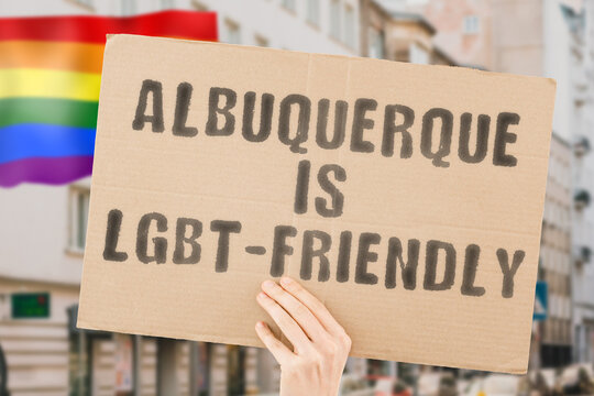 The phrase " Albuquerque is LGBT-Friendly " on a banner in men's hand with blurred LGBT flag on the background. Human relationships. different. Diverse. liberty. Sexuality. Social issues. Society