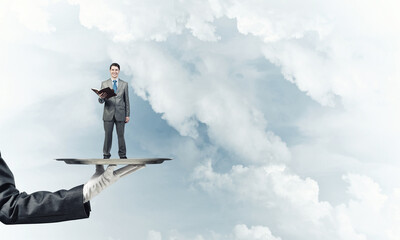 Businessman on metal tray with red book in hands against blue sky background