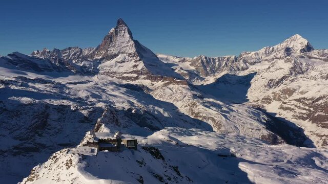 Aerial drone footage of the Matterhorn and the gornergrat ridge with its observatory and hotel above Zermatt in the alps in Switzerland on a sunny winter day. Shot with a rotation motion