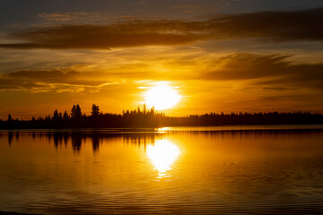 Fototapeta na wymiar Orange and Yellow sunset over lake with Black silhouetted tree line