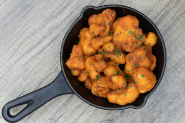 Overhead view of spicy and breaded buffalo cauliflower nuggets to eat out of the cast iron pan as...