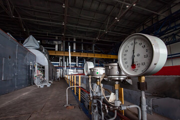 Machine room of heat power station. Grey generator machine left, out of focus. Manometers gauges right in focus. Metal floor and ceiling. Karagandy, Kazakhstan.