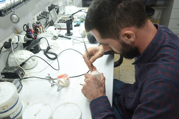 A young man at a desk in the workshop of a dental technician in the laboratory makes parts for dentistry