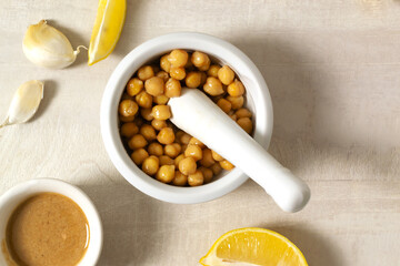 Fototapeta na wymiar Add boiled chickpeas to Garlic with lemon juice in a ceramic mortar. Ingredients for making hummus. Boiled chickpeas, tahini, garlic, lemon and butter. A traditional Middle Eastern dish. Top view.