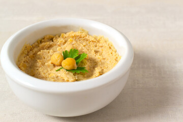 Hummus in a ceramic white bowl with a parsley leaf on a light background. A traditional Middle Eastern dish. Horizontal orientation. Healthy nutrition concept.