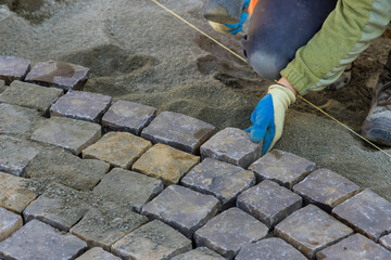 Road master of gloves lays paving stones in layers stone road by professional worker using hammer