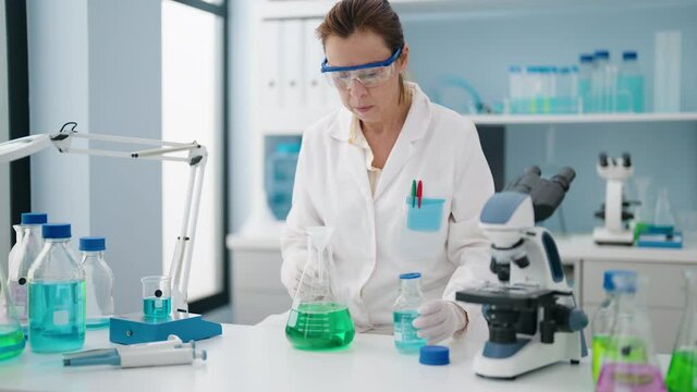Middle age woman wearing scientist uniform measuring liquid at laboratory